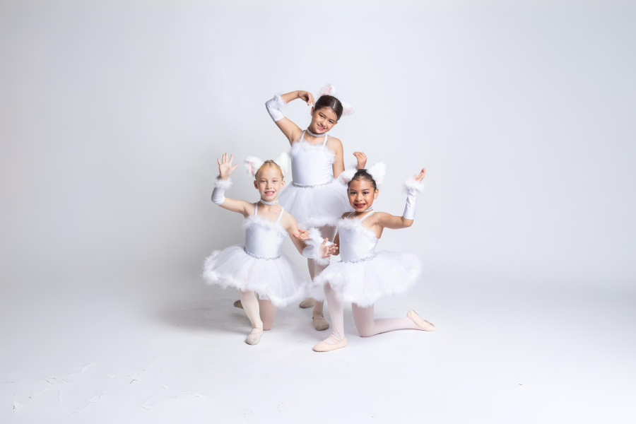 Three young girls dressed in white cat-themed ballet costumes pose playfully against a white background.